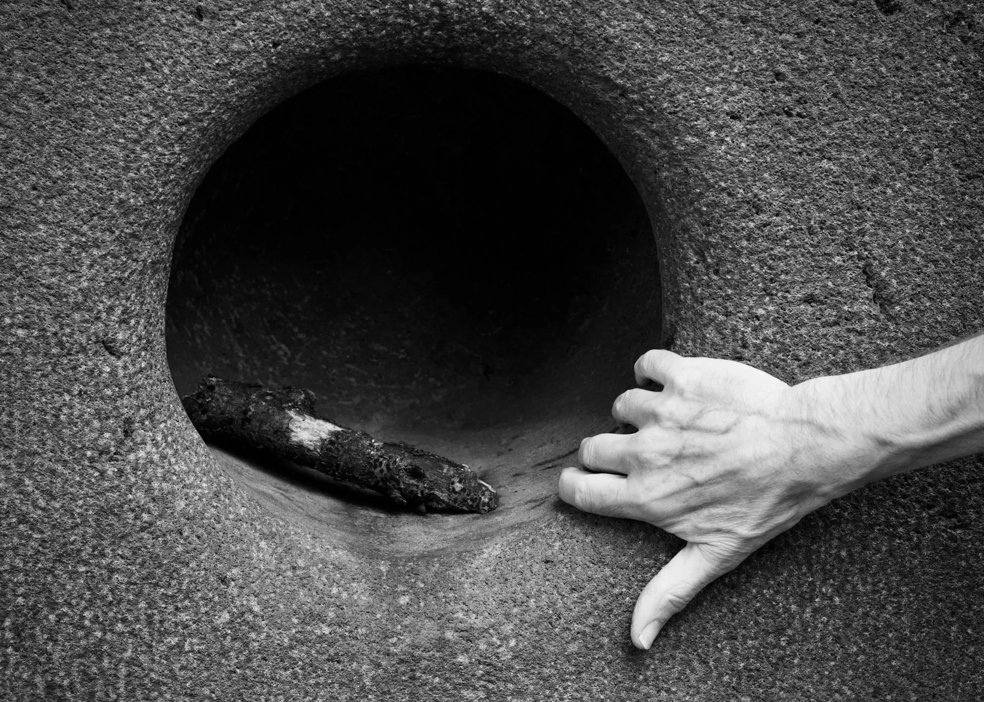A hand beside a round hole at the base of a concrete wall, the kind of gap mice and rats use to get in