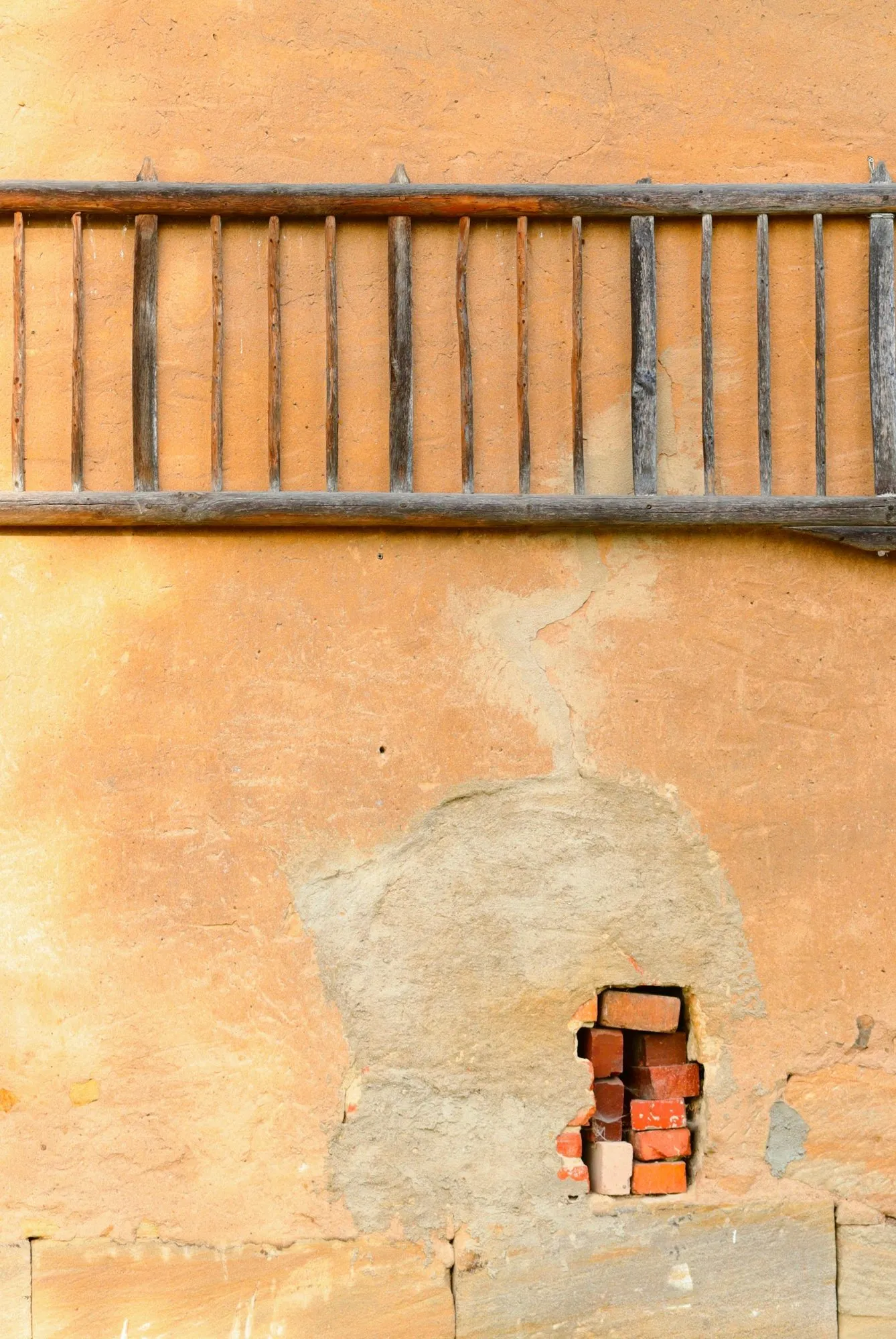 A patch of missing render at the base of a wall, exposing a gap in the brickwork