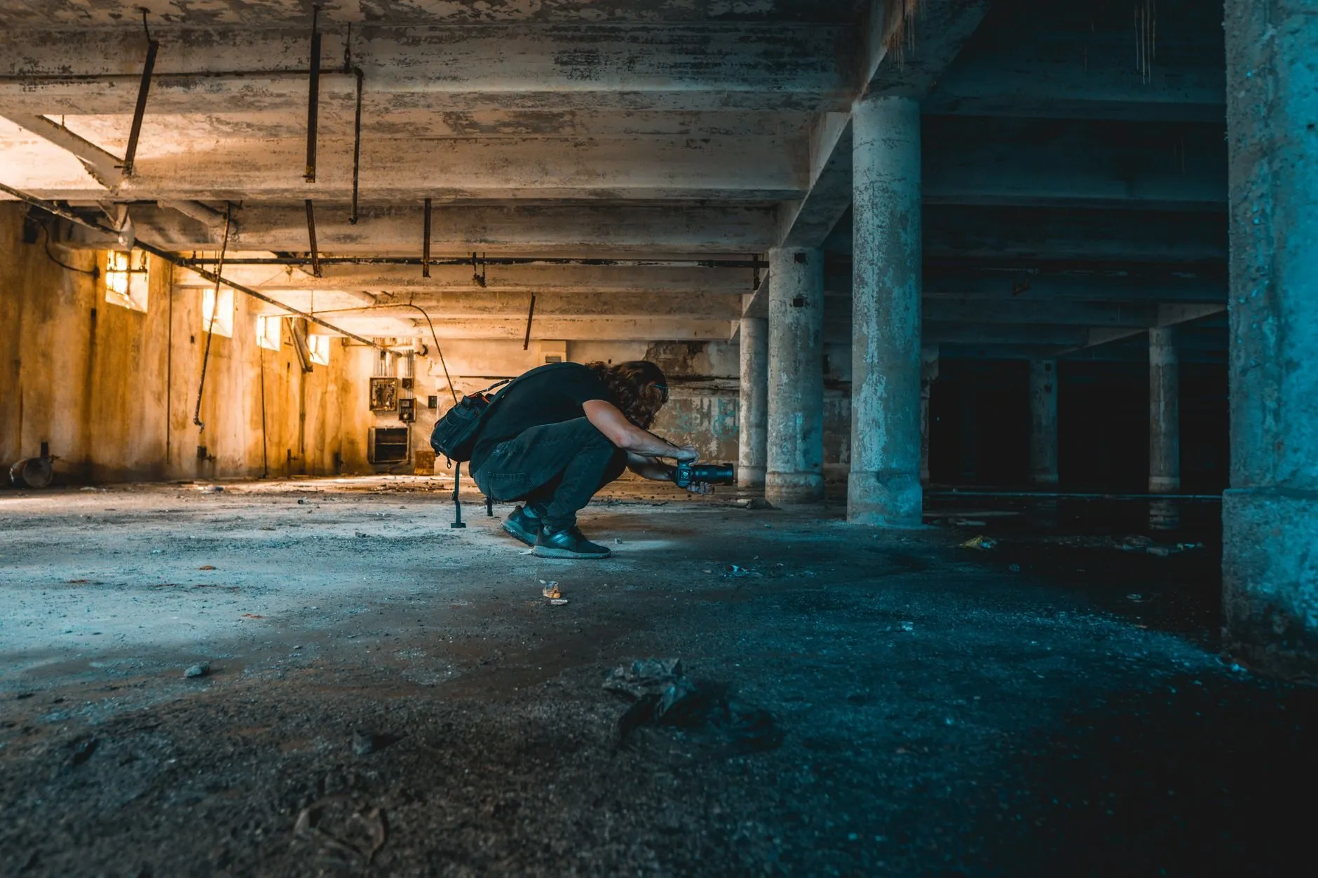 A technician crouched with a torch in a dark basement, checking along the floor and walls