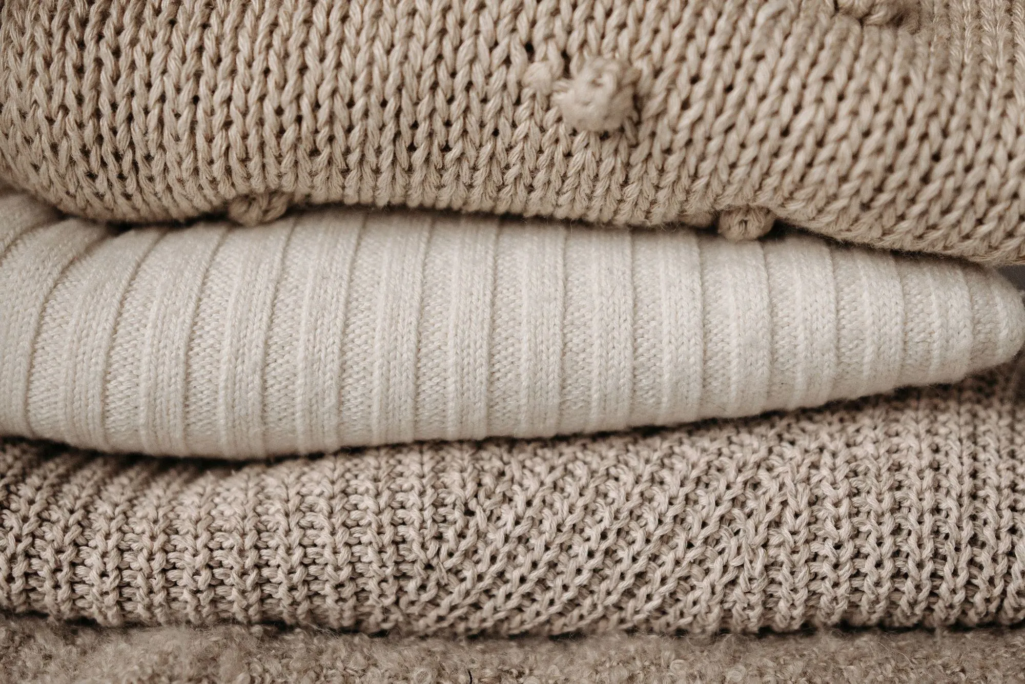 A stack of folded wool and cotton jumpers in beige and cream
