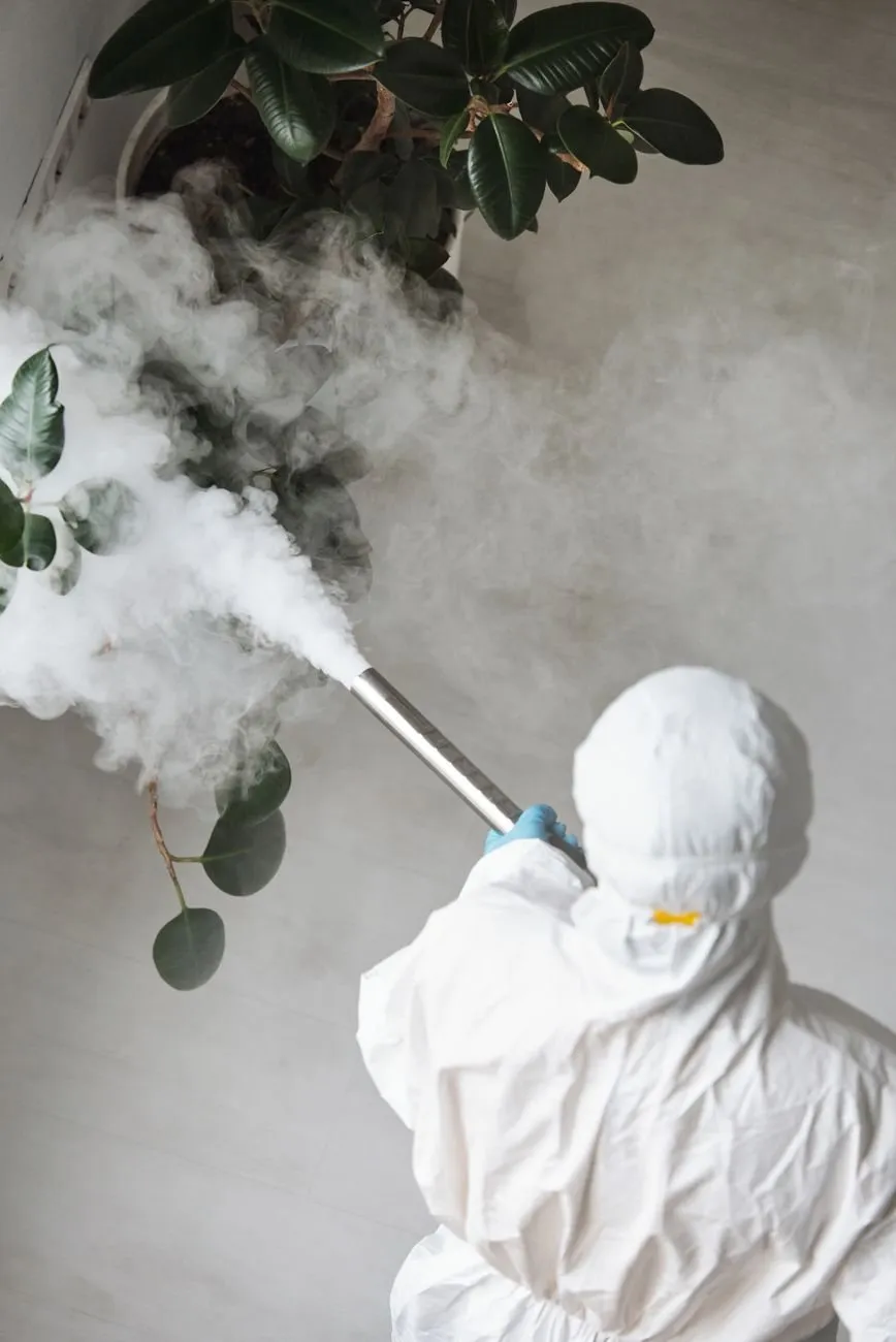 A technician in a white suit, seen from behind, fogging a room
