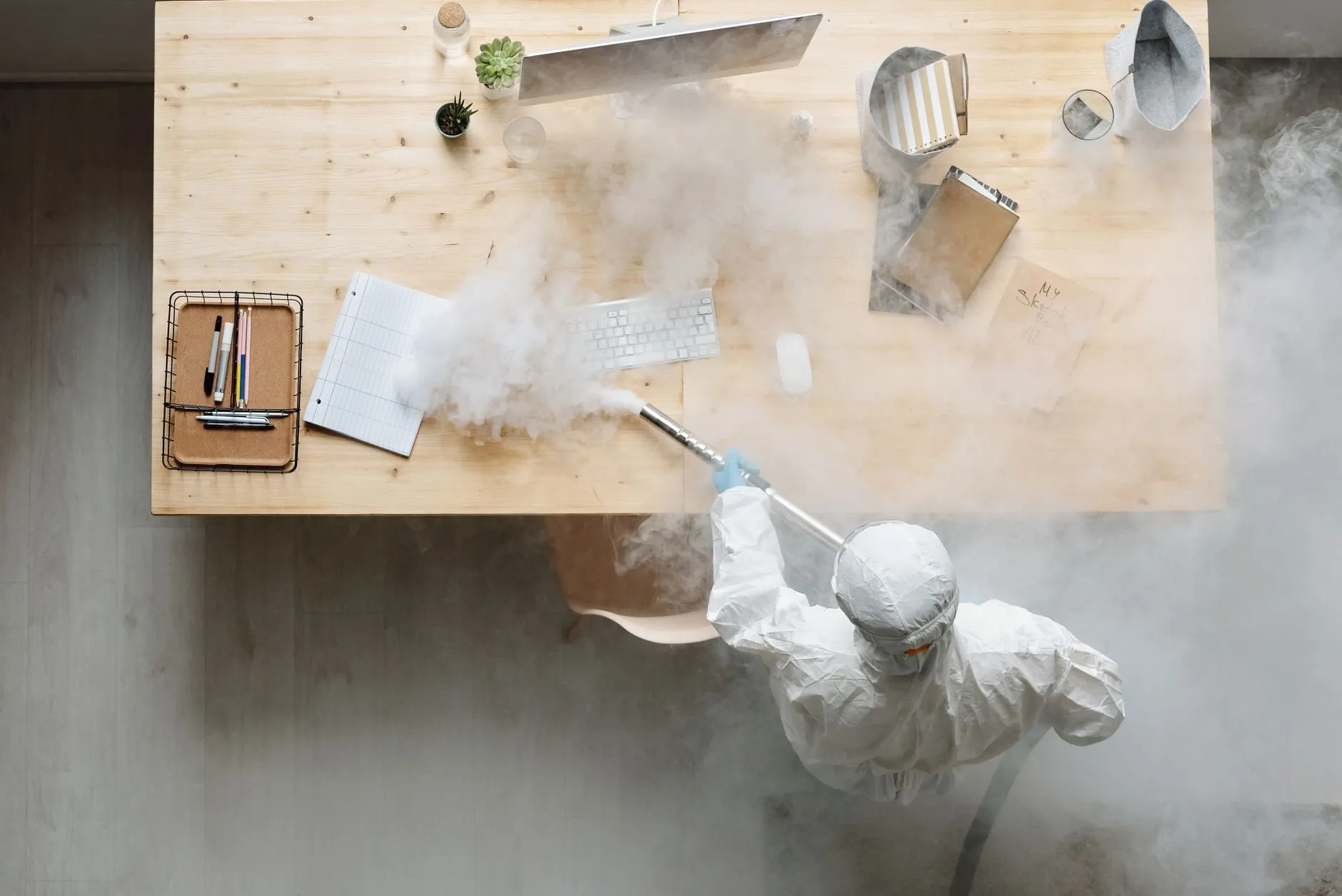 Overhead view of a technician in a white suit treating the area under an office desk